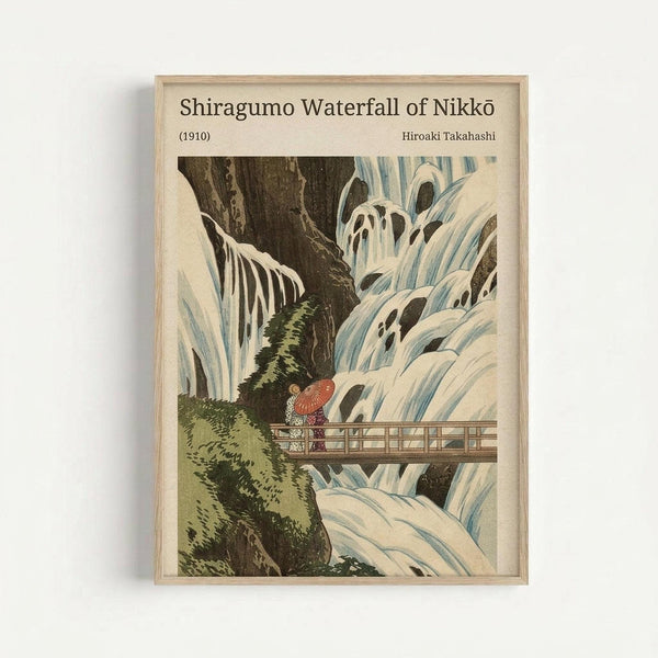 Vintage Japanese woodblock print artwork depicting Shiragumo Waterfall with cascading white and blue water flowing over dark rocky cliffs. Two figures in traditional dress with a red umbrella stand on a wooden bridge spanning the gorge, surrounded by green moss-covered rocks. The print is displayed in a light wooden frame against a white wall, showing the classic ukiyo-e art style with muted earth tones and delicate line work typical of early 1900s Japanese prints.