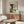 May include: Japanese woodblock print artwork depicting a dramatic waterfall with cascading white and blue water, wooden bridge, and green foliage, displayed in a thin wooden frame above a mid-century modern walnut credenza. The vintage-style poster is shown in a bright, minimalist living room with white walls, cream upholstered chair, glass coffee table, and modern table lamp.