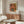 May include: Framed poster print of roses in a blue vase displayed above a wooden sideboard in a modern living room. The artwork shows pink and coral colored roses painted in an impressionist style. White upholstered chair, glass coffee table, and wooden floor lamp visible in the minimalist interior setting with cream walls.