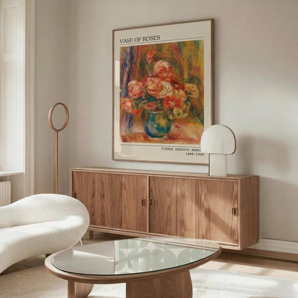 May include: Framed poster print of roses in a blue vase displayed above a wooden sideboard in a modern living room. The artwork shows pink and coral colored roses painted in an impressionist style. White upholstered chair, glass coffee table, and wooden floor lamp visible in the minimalist interior setting with cream walls.