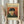 May include: Person in cream clothing holds framed Van Gogh museum poster featuring self-portrait with bandaged ear and pipe. Poster shows artist in green coat and fur hat against orange-red background. Cream-colored frame and pampas grass visible in soft, neutral-toned room setting.