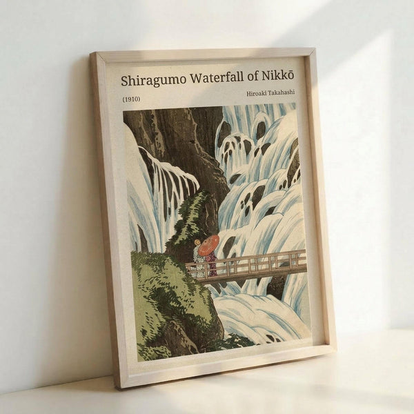 May include: Framed vintage Japanese woodblock print reproduction showing Shiragumo Waterfall with cascading white and blue water flowing over dark rocky cliffs. Two figures with traditional red umbrella stand on wooden bridge crossing the falls. Green moss and vegetation accent the dramatic landscape. Light wooden frame displayed against white wall, leaning on surface.