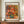 May include: Framed art print of an impressionist-style floral painting featuring pink and coral roses in a blue-green vase, displayed on a wooden sideboard against white wainscoting. The poster shows "VASE OF ROSES" at the top and "PIERRE AUGUSTE RENOIR 1890-1900" at the bottom in a thin brown frame. A small white ceramic vase and stacked books sit nearby on the warm wood surface.