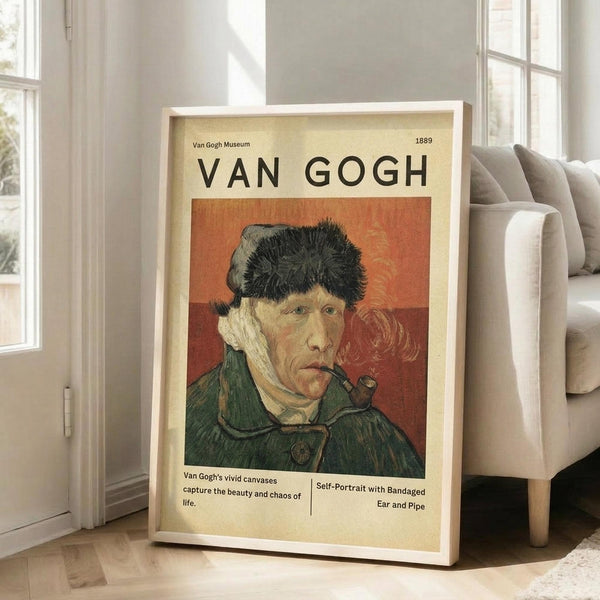 May include: A framed Van Gogh museum exhibition poster featuring a self-portrait of the artist wearing a dark fur hat and green coat while smoking a pipe, set against an orange-red background. The vintage-style poster has cream borders with museum text and is displayed in a light wood frame, leaning against a beige upholstered chair in a bright, minimalist room with white walls and large windows.