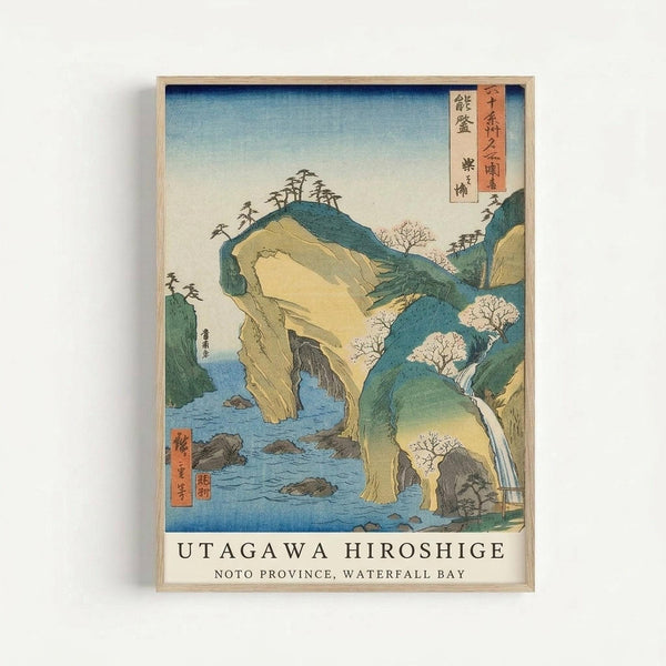 Framed Japanese woodblock print showing a dramatic coastal landscape with steep cliffs and rock formations jutting from blue water. The artwork features muted green, yellow and blue tones depicting rugged terrain with sparse trees on clifftops and a waterfall cascading down the rocks. Traditional Japanese text appears in red cartouches in the upper right corner, with additional text on the left side. The print is displayed in a simple light wood frame against a white background, with English tex