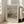 May include: Framed Van Gogh museum poster showing weathered fishing boats pulled up on a sandy beach. The muted earth-toned artwork depicts several wooden vessels with tall masts against an overcast sky. The poster features clean typography and museum-style layout with descriptive text below the painting. Light wood frame leans against white wall next to beige upholstered chair in bright, minimalist room with large windows.