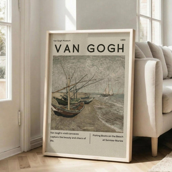 May include: Framed Van Gogh museum poster showing weathered fishing boats pulled up on a sandy beach. The muted earth-toned artwork depicts several wooden vessels with tall masts against an overcast sky. The poster features clean typography and museum-style layout with descriptive text below the painting. Light wood frame leans against white wall next to beige upholstered chair in bright, minimalist room with large windows.