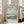May include: Japanese woodblock print reproduction in light wood frame leaning against white wall next to beige upholstered chair. Artwork shows cherry blossoms framing Mount Fuji view across blue water with boats and green shoreline. Soft natural lighting from nearby windows creates gentle shadows on hardwood floor.