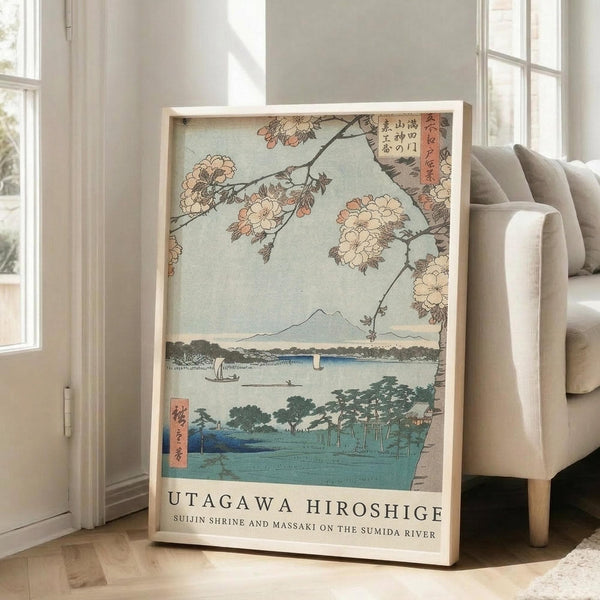 May include: Japanese woodblock print reproduction in light wood frame leaning against white wall next to beige upholstered chair. Artwork shows cherry blossoms framing Mount Fuji view across blue water with boats and green shoreline. Soft natural lighting from nearby windows creates gentle shadows on hardwood floor.