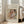 May include: Framed art print leaning against beige armchair in bright living room with white walls and windows. Print shows Renoir's soft pastel painting of woman in white dress holding blonde child in red clothing, with text identifying artist and artwork title. Natural wood frame, textured cream matting.