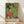 May include: Framed poster print of traditional Japanese artwork featuring a monk in red robes riding a tiger, surrounded by various animals and mythological creatures on a green geometric patterned background. The wooden-framed print leans against a white wall on light wood flooring, with natural sunlight creating soft shadows across the scene.