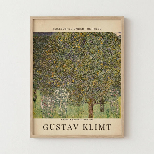 May include: Framed art print displayed on white wall showing Gustav Klimt's pointillist-style painting of flowering trees with dense, textured canopy in greens, yellows and purples above grass with scattered pink roses. Museum exhibition poster format with cream background and black text identifying the artwork and artist. Light wood frame.