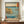 May include: Framed Japanese woodblock print depicting a coastal scene with rocky cliffs, turquoise waters, small boats, and Mount Fuji in the distance. The artwork features traditional ukiyo-e style with muted earth tones and blue gradients. Displayed on a wooden sideboard alongside a white ceramic vase and stack of books against white paneled walls in a modern interior setting.
