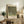 May include: Framed art print displaying Gustav Klimt's pointillist-style painting of dense green foliage and rosebushes with Museum of Modern Art New York attribution, positioned on rustic wooden sideboard alongside fern plant, ceramic vase, stacked books, and cream upholstered chair in neutral-toned living room setting