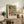 May include: Framed Japanese woodblock print featuring figures in colorful robes with tigers and other animals on green geometric background, displayed on rustic wooden sideboard alongside fern plant, ceramic vase, and books in neutral-toned living room setting with beige upholstered furniture