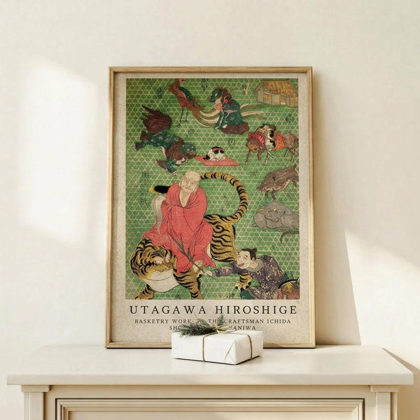 May include: Framed Japanese woodblock print featuring figures in traditional dress with animals including a tiger, set against green geometric background. Light wood frame sits on pale wooden surface beside small white wrapped gift. Minimalist neutral wall setting with soft natural lighting.