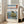 May include: Framed Japanese woodblock print showing rocky coastal cliffs jutting from blue ocean waters with Mount Fuji visible on distant horizon under pale sky. Print features traditional ukiyo-e art style with red Japanese text cartouches, displayed in light wood frame leaning against white wall next to beige upholstered sofa in bright modern living room with large windows.