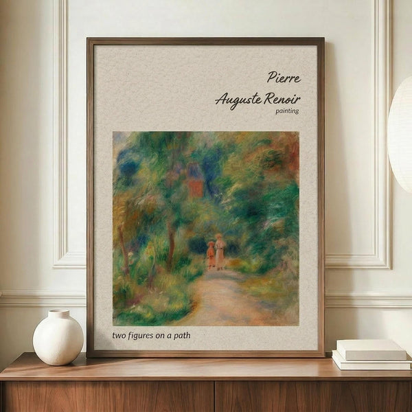 May include: Framed reproduction of Renoir's impressionist painting showing two small figures walking along a winding path through lush green foliage with dappled light filtering through trees. The artwork features soft brushstrokes in greens, blues, oranges and earth tones. Displayed in a thin brown frame on a wooden sideboard next to a cream ceramic vase and white books against cream paneled walls.