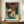 May include: Framed Japanese woodblock print featuring autumn maple trees with vibrant red-orange foliage overlooking a turquoise waterfall cascading down white limestone cliffs. The traditional ukiyo-e artwork shows distant mountains and includes Japanese text cartouches. The brown-framed poster sits on a wooden sideboard next to a white ceramic vase and books in a bright room with white walls and decorative molding.