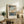 May include: Framed Japanese woodblock print featuring autumn maple trees with orange leaves overlooking a blue water landscape, displayed on rustic wooden sideboard alongside fern plant, ceramic vase, and books in neutral-toned living room setting