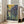 May include: Framed Van Gogh Irises poster print leaning against white wall near beige upholstered chair. Artwork features purple and blue iris flowers with flowing green stems against golden yellow background in signature post-impressionist style. Light wood frame, bright sunlit room with large windows and hardwood floors.