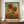 May include: Framed sunflower artwork in Van Gogh's distinctive swirling style displayed on wooden sideboard against cream wainscoted wall. The painting shows two large golden sunflowers with brown centers and flowing petals against blue sky with pale sun. Rich brushstrokes create movement in the orange-brown field below. White ceramic vase and stack of books sit alongside the brown-framed print.