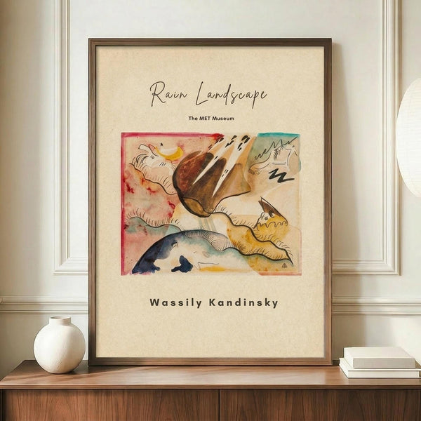 May include: Framed poster featuring Kandinsky's abstract watercolor painting with flowing organic forms in browns, yellows, blues and reds on cream background. Modern wood frame displayed on wooden sideboard next to white ceramic vase and stacked books against white wainscoted wall.