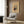 May include: Framed Kandinsky abstract art print with colorful geometric shapes on beige background, displayed on wood paneled wall above beige upholstered armchair with patterned pillow. Modern brass floor lamp and dark round side table with open book visible in neutral-toned living room setting.