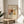 May include: Framed art print featuring abstract watercolor painting with flowing organic forms in warm browns, yellows, blues and coral tones. The piece displays flowing lines and cloud-like shapes characteristic of early abstract art. Print is displayed in thin wooden frame on round wooden side table next to beige upholstered chair, with plant leaves visible in soft natural lighting.