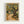 May include: Framed Van Gogh reproduction print hanging on white wall, showing impressionist landscape with gnarled olive tree, winding dirt path, and small house. Thick brushstrokes create textured appearance in yellows, greens, and earth tones. Light wood frame with cream matting displays the classic post-impressionist artwork in modern interior setting.