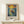 May include: Framed art print displayed on light wood shelf against cream wall, showing figure standing in wooden boat on water with swirling golden sun and starry sky in Van Gogh's distinctive brushstroke style. Text below reads "Vincent Van Gogh" with French subtitle. Small wrapped gift box with twine sits beside the natural wood frame.