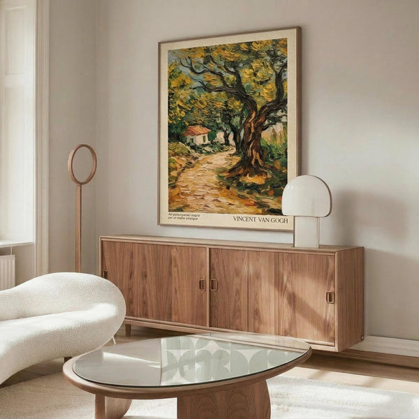 May include: A framed Van Gogh olive trees poster displayed above a walnut wood credenza in a minimalist living room. The artwork shows swirling brushstrokes in golden yellow and green tones depicting gnarled olive trees along a winding path with a small house in the background. The room features a white sculptural chair, glass-top oval coffee table, and warm wood furnishings against neutral walls.