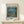 May include: Framed Van Gogh museum poster showing Starry Night Over the Rhone painting with swirling blue night sky, golden stars, and reflections on water. Light wood frame displayed on white wooden console table with small wrapped gift box with natural twine and pine sprig. Clean minimal styling against cream wall with soft natural lighting.