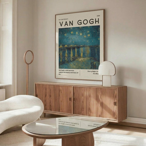 May include: Van Gogh museum poster featuring Starry Night Over the Rhone painting with swirling blue night sky, yellow stars, and water reflections, displayed in thin brown frame above wooden sideboard with sliding doors. Modern living room setting with white curved chair, round glass coffee table, brass floor lamp, and white table lamp on credenza.