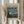 May include: Person in cream blouse holding framed Van Gogh museum poster featuring The Starry Night painting with swirling blue sky and yellow stars. Natural wood frame, beige mat, dried wheat stems visible. Soft window lighting creates gentle shadows on neutral wall background.