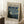 May include: Museum-style poster featuring Van Gogh's Starry Night painting with swirling blue sky, yellow stars, and dark cypress tree, displayed in light wood frame leaning against white wall corner. White coffee cup sits on wooden block nearby on textured cream rug. Poster shows beige background with black text and 1889 date.