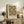 May include: Framed botanical art print featuring green and cream chrysanthemum floral pattern displayed on rustic wooden sideboard beside fern plant, ceramic vase, and books in warm neutral living room setting with beige chair and lamp
