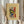 May include: Hands holding framed abstract art print featuring vibrant swirling brushstrokes in green, red, blue, yellow and orange colors. Cream-colored mat with beige wooden frame. Person wearing beige ruffled sleeve top holds decorative dried wheat stems. Soft natural lighting against neutral curtained background.