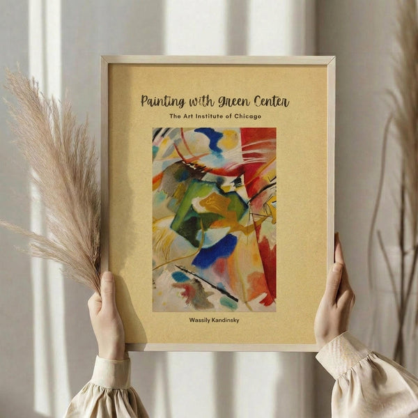 May include: Hands holding framed abstract art print featuring vibrant swirling brushstrokes in green, red, blue, yellow and orange colors. Cream-colored mat with beige wooden frame. Person wearing beige ruffled sleeve top holds decorative dried wheat stems. Soft natural lighting against neutral curtained background.
