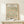 May include: Framed botanical art print featuring William Morris daisy pattern with green foliage and orange-red flowers on cream background, displayed on light wood console table beside white wrapped gift with evergreen sprig, against neutral wall in minimalist home setting