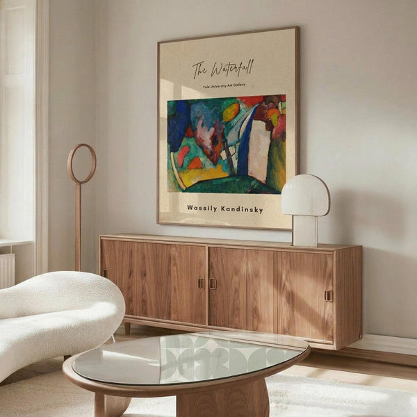 May include: Abstract colorful poster print featuring vibrant blues, greens, reds, and yellows in Kandinsky's expressionist style, displayed in thin wooden frame above walnut credenza. Modern living room setting with cream curved chair, glass oval coffee table, and white table lamp. Warm natural lighting creates shadows across minimalist neutral decor.