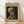 May include: Framed museum-style poster featuring Van Gogh's painting of a human skull with cigarette in mouth, displayed against white wall on light wood flooring. The artwork shows pale yellow and brown tones on dark background, housed in natural wood frame with cream matting and museum exhibition text.