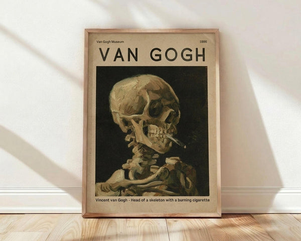 May include: Framed museum-style poster featuring Van Gogh's painting of a human skull with cigarette in mouth, displayed against white wall on light wood flooring. The artwork shows pale yellow and brown tones on dark background, housed in natural wood frame with cream matting and museum exhibition text.