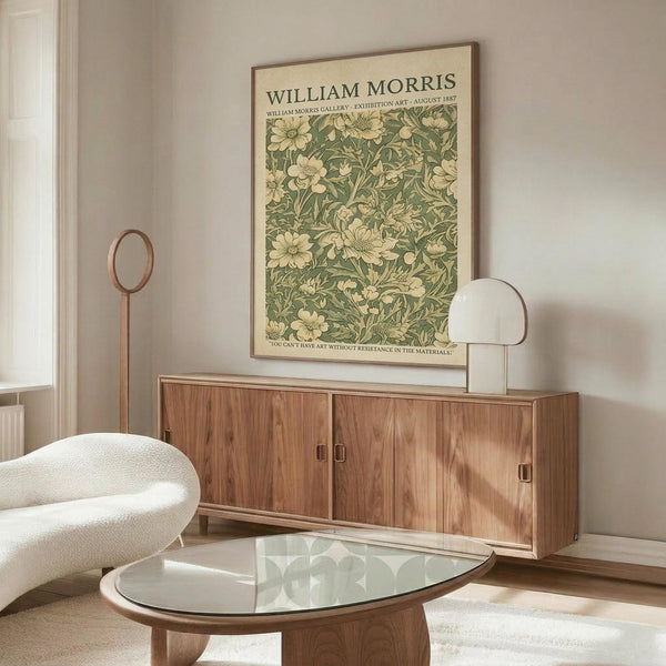 May include: Vintage botanical poster with William Morris floral pattern in sage green and cream tones, displayed above mid-century walnut credenza in bright modern living room. White curved chair and glass oval coffee table visible, with minimalist copper accent lighting and neutral wall colors.
