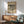 May include: Framed Kandinsky abstract art print with black line drawings on cream background, displayed above mid-century modern wood credenza with white ceramic lamp. Sage green upholstered armchair with wooden frame sits nearby on hardwood floor. Natural sunlight creates geometric shadows on white wall in minimalist living room setting.