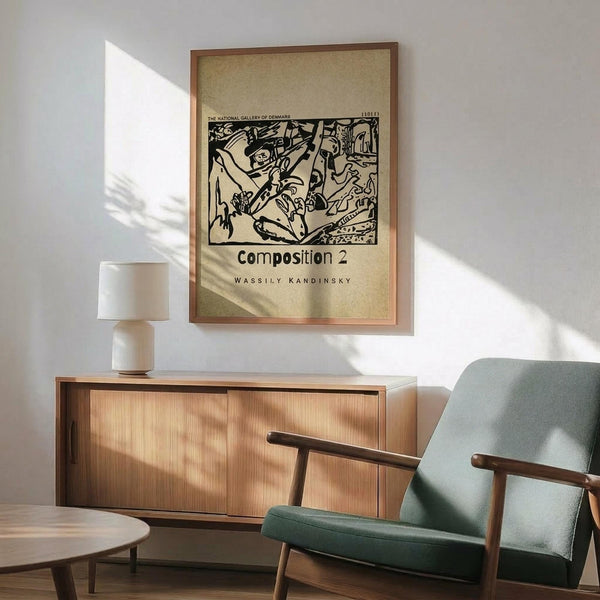 May include: Framed Kandinsky abstract art print with black line drawings on cream background, displayed above mid-century modern wood credenza with white ceramic lamp. Sage green upholstered armchair with wooden frame sits nearby on hardwood floor. Natural sunlight creates geometric shadows on white wall in minimalist living room setting.