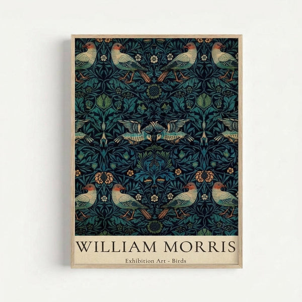 Framed art print featuring William Morris's intricate pattern design with birds and botanical elements on a dark teal background. The symmetrical pattern shows colorful birds with green, orange and cream plumage among detailed foliage, flowers and vines. Text at bottom reads "WILLIAM MORRIS Exhibition Art - Birds" on cream background. Light wood frame displayed against white wall.