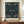 May include: Framed William Morris exhibition poster featuring intricate pattern of birds and foliage in deep blues and greens, displayed on wooden credenza beside white ceramic vase and stacked books against cream paneled wall