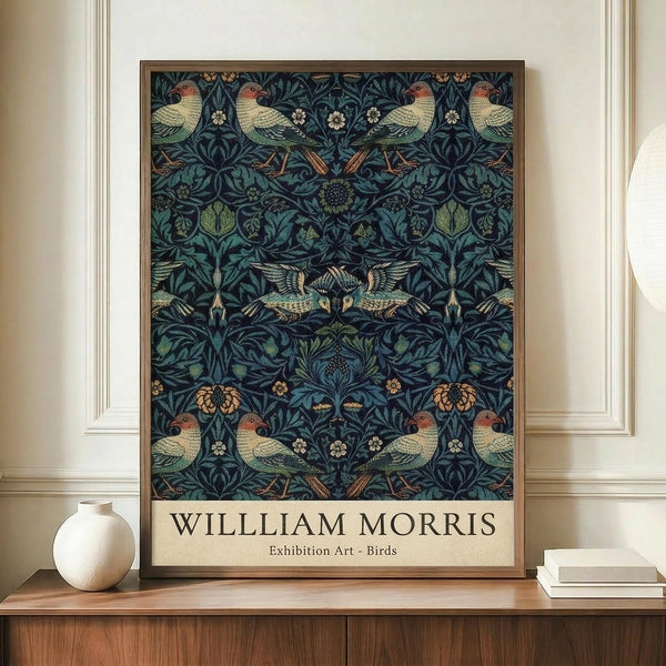 May include: Framed William Morris exhibition poster featuring intricate pattern of birds and foliage in deep blues and greens, displayed on wooden credenza beside white ceramic vase and stacked books against cream paneled wall