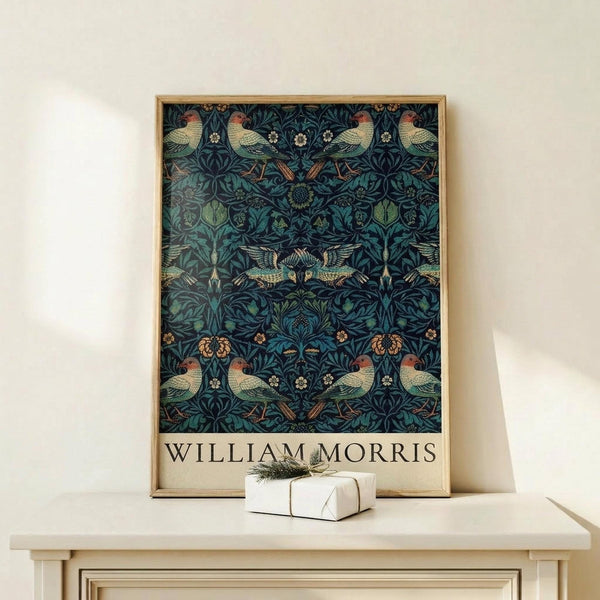 May include: Framed poster featuring William Morris-style pattern with birds and botanical motifs in deep blues and greens, displayed on light wood furniture beside small wrapped gift with twine and greenery sprig against cream wall